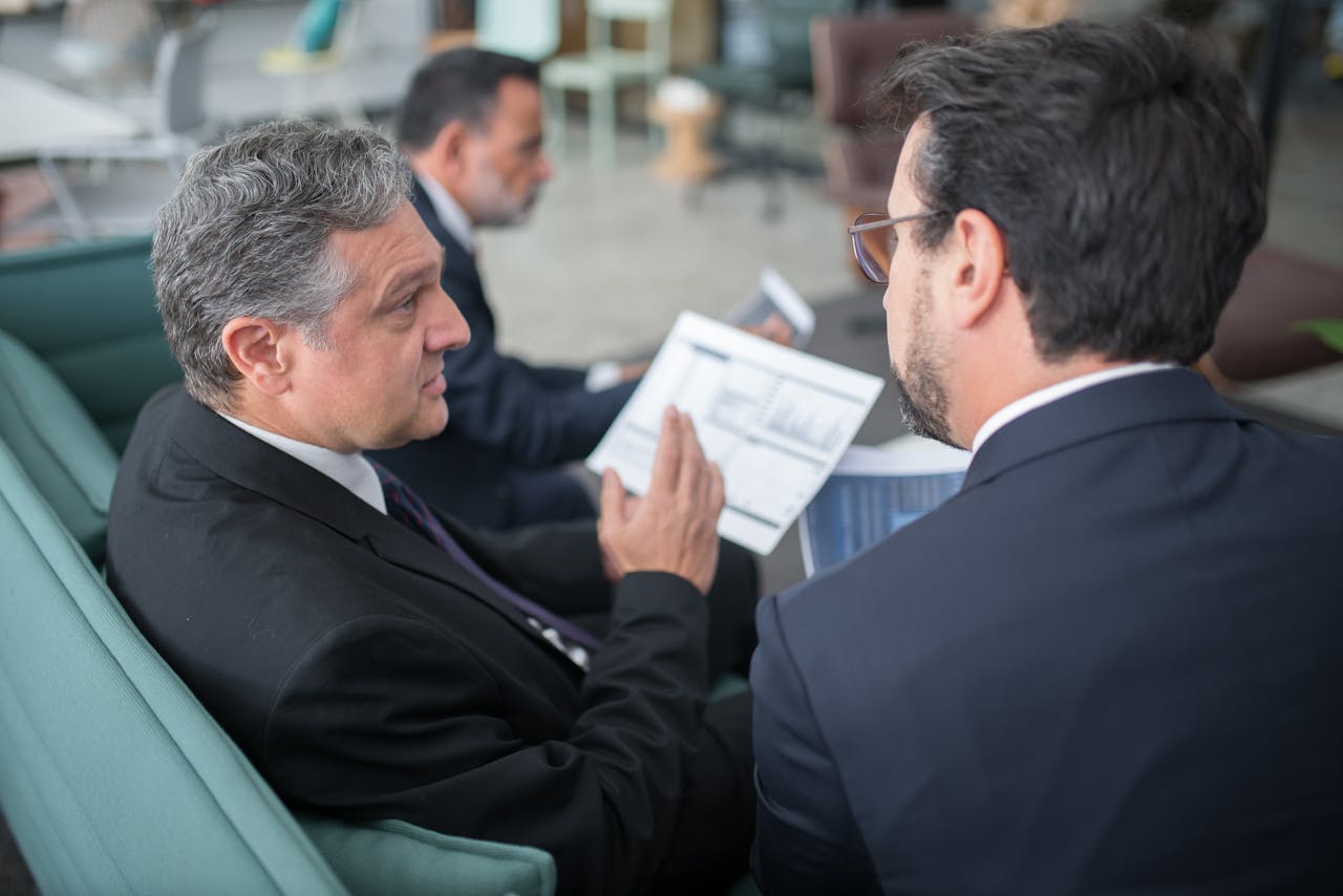 Home Two businessmen engaged in a discussion, examining reports in a modern office environment.